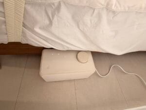 침대 옆 바닥에 설치된 나비엔 온수매트 본체와 연결된 호스가 보이는 실물 사진